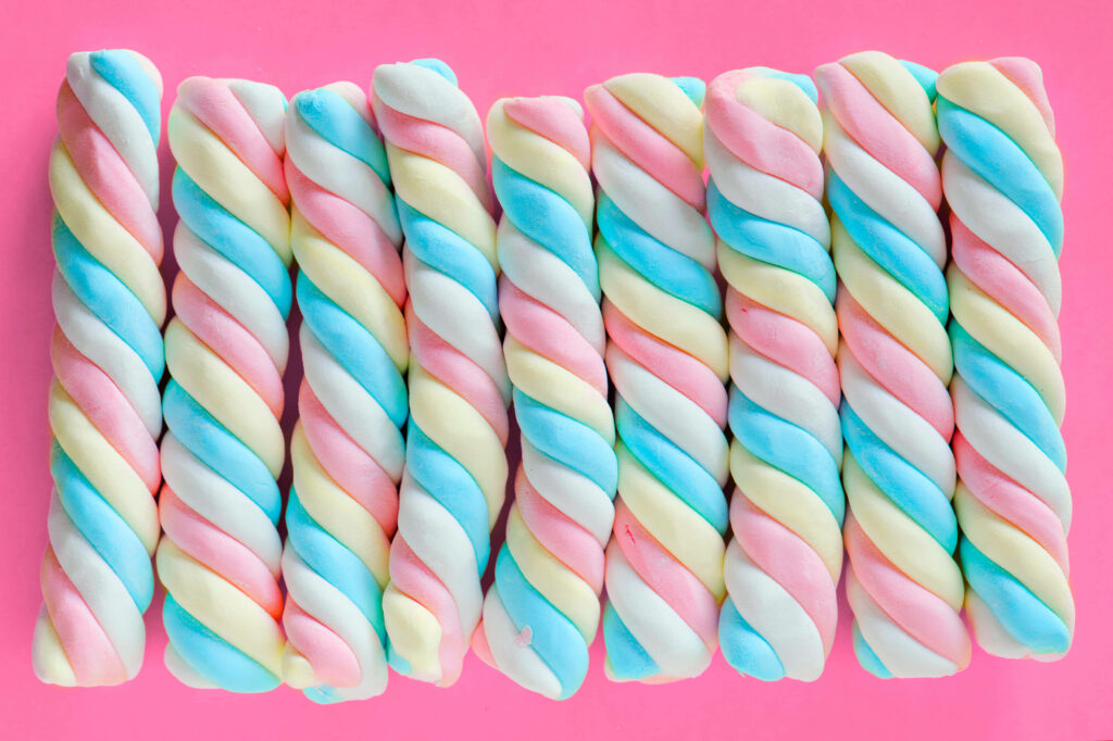 Twisted pastel marshmallows in pink blue yellow and white on vibrant pink wallpaper background