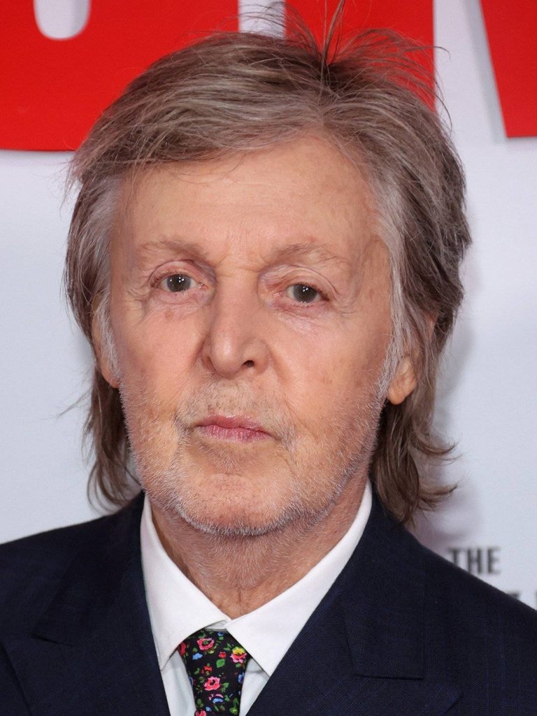 High-definition portrait of Paul McCartney in dark suit and floral tie on vibrant red backdrop phone wallpaper