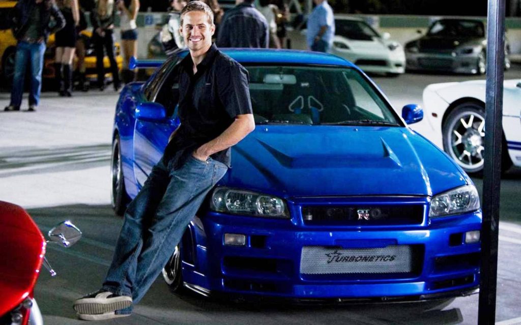 Paul Walker leaning on blue Nissan Skyline GT-R R34 at nighttime Fast and Furious street race Wallpaper