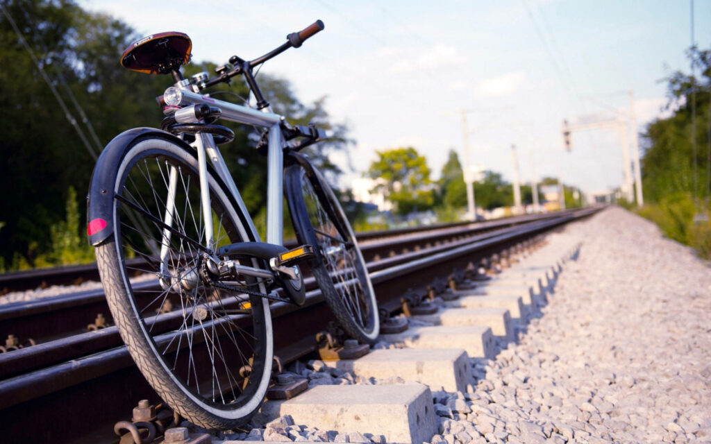 Sleek bicycle parked by sunlit train tracks with lush greenery peaceful travel adventure wallpaper