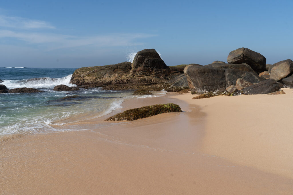 Smooth stones on sandy beach with gentle waves and clear blue sky calming coastal wallpaper