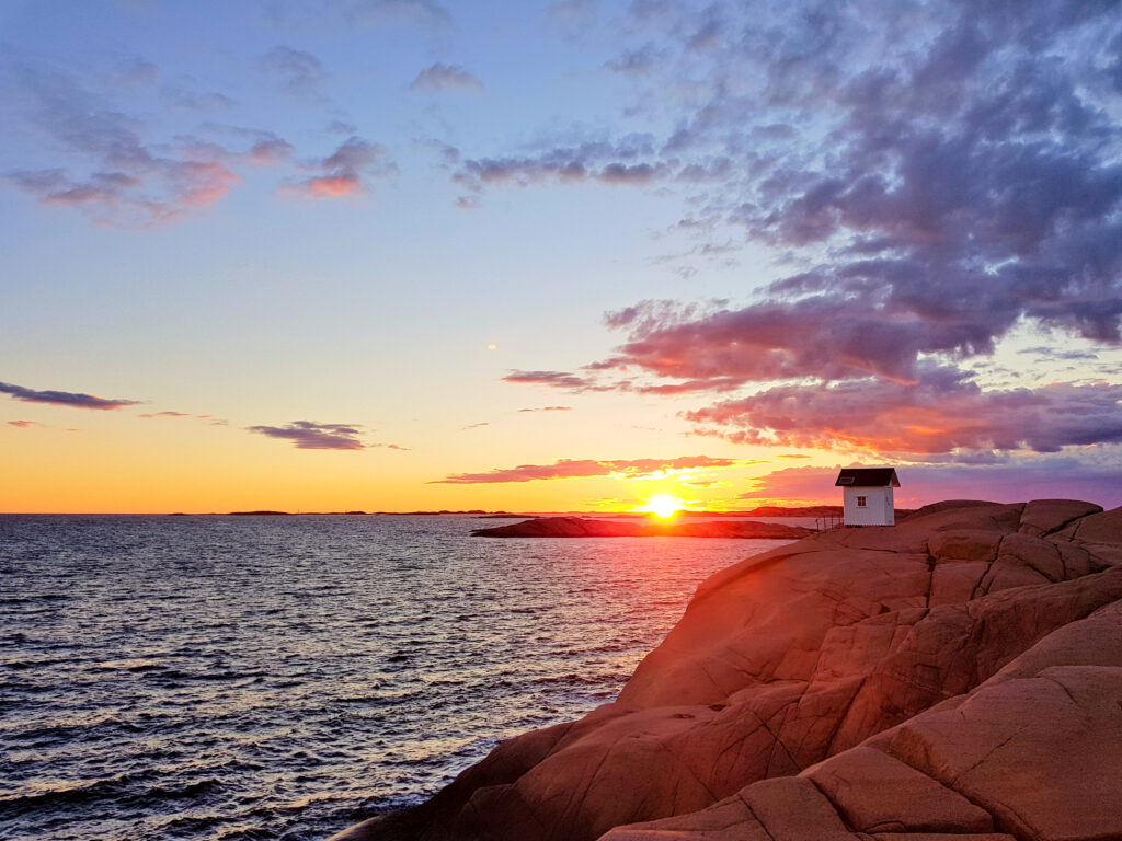 Coastal hut on rocky shore at golden sunset with vibrant orange purple and blue sky background Wallpaper