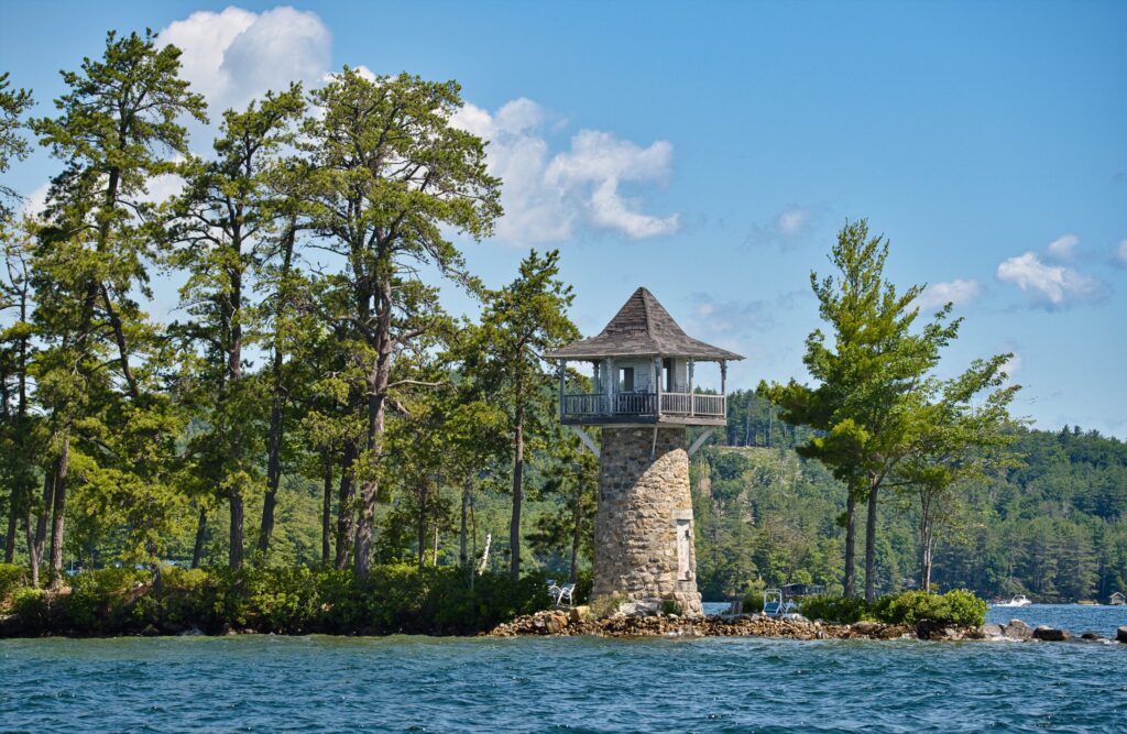 Stone lighthouse on island with green trees and blue sea under bright sky coastal wallpaper