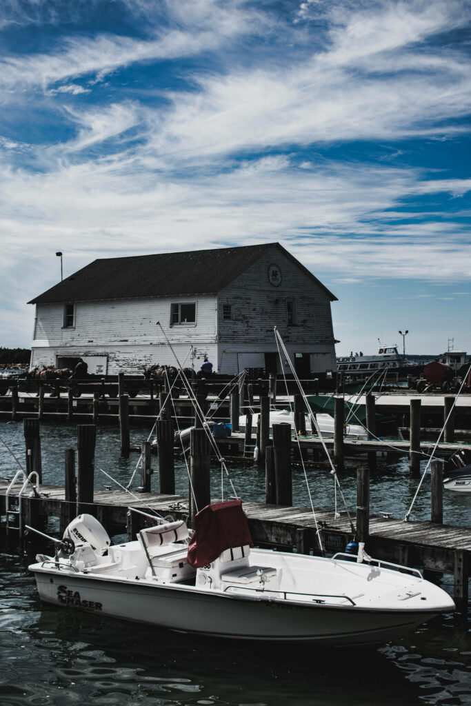 Small white boat docked in peaceful harbor near rustic wooden building under dramatic swirling clouds Wallpaper