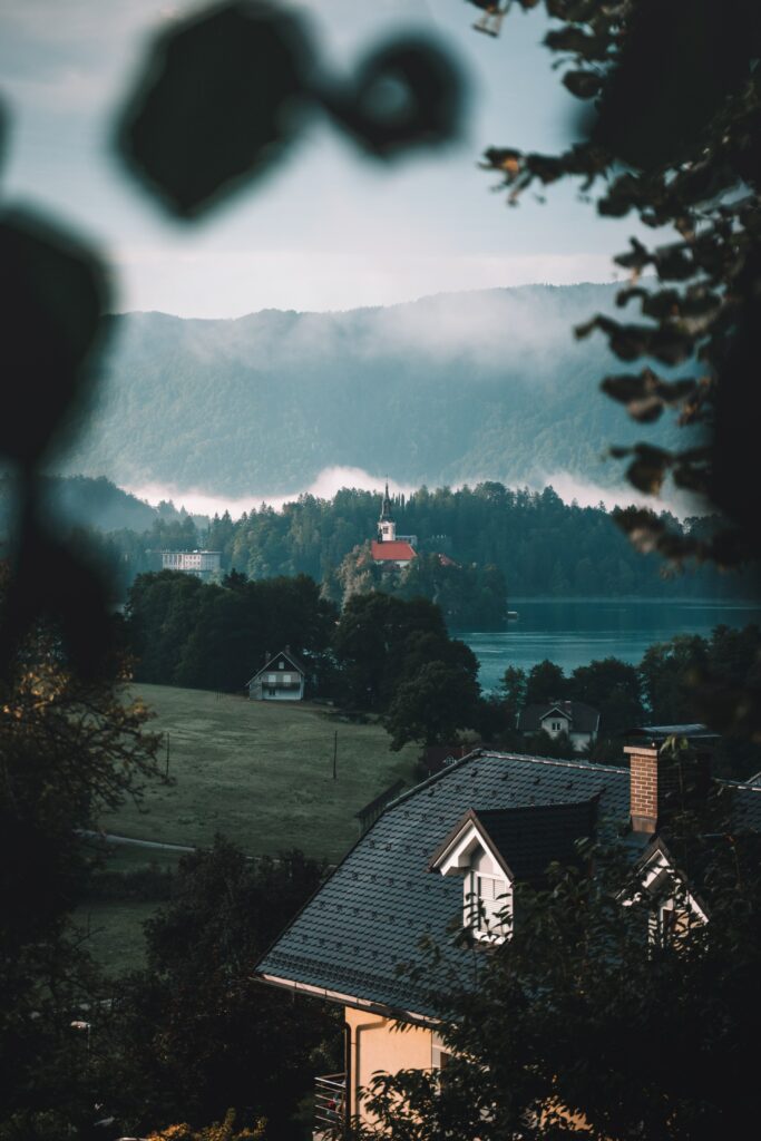 Charming houses by tranquil lake with lush greenery and misty mountains serene nature wallpaper
