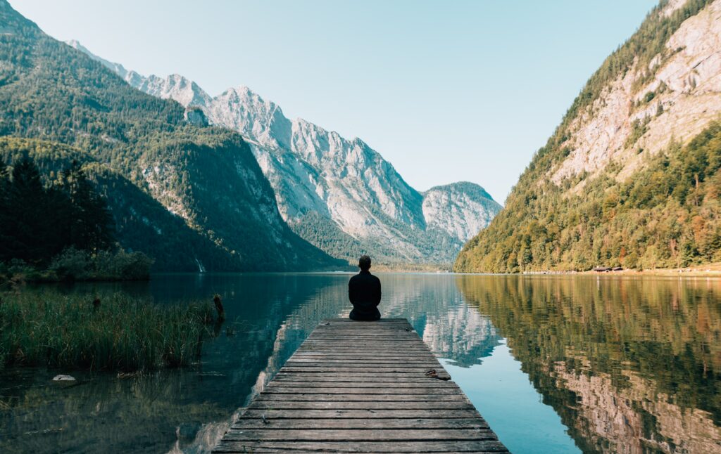 Solitary person on wooden pier overlooking tranquil lake with mountains and lush greenery calm Wallpaper