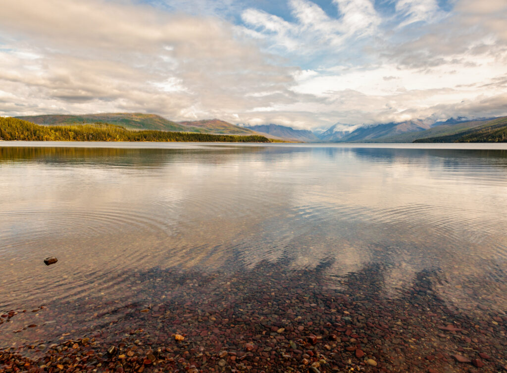 Serene lake with gentle ripples in lush valley mountains under soft cloudy sky wallpaper background