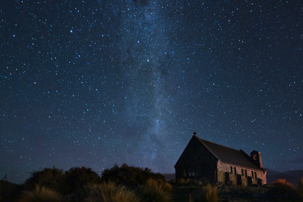 Peaceful rural house silhouette under a swirling starry galaxy sky with deep blue hues wallpaper