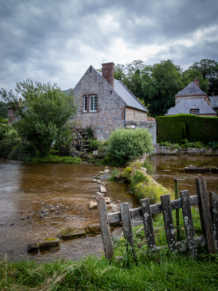 Charming stone house by river with waterwheel lush trees cloudy sky rustic countryside scene Wallpaper