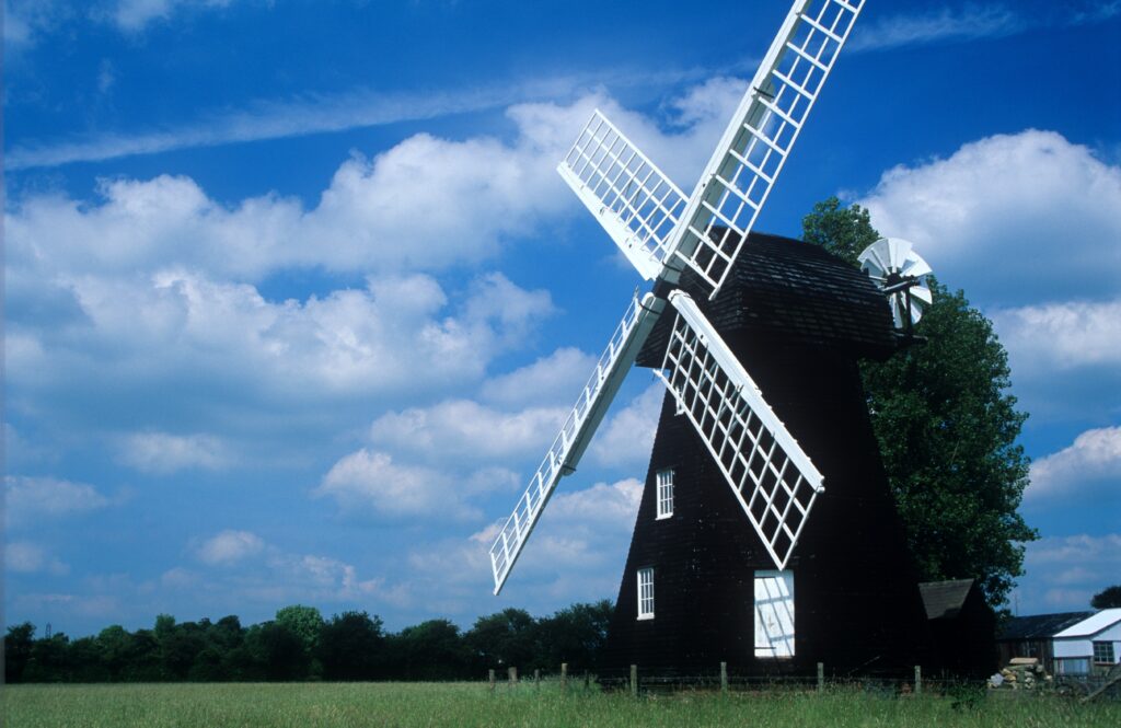 Classic windmill in green summer field under blue sky with white clouds peaceful rural wallpaper