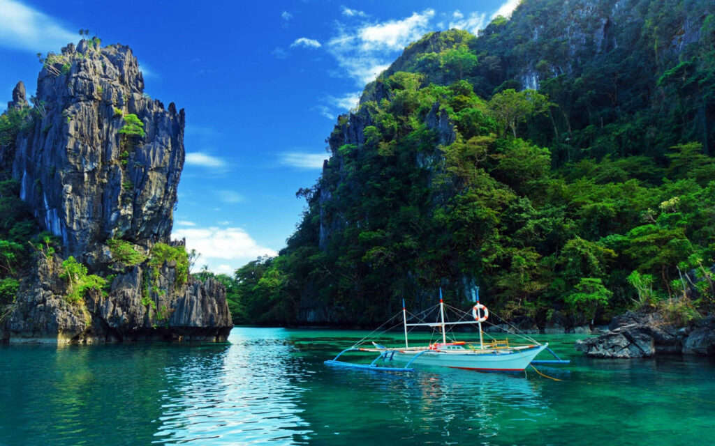 Traditional boat on clear tropical water near green cliffs and rocky island formations wallpaper