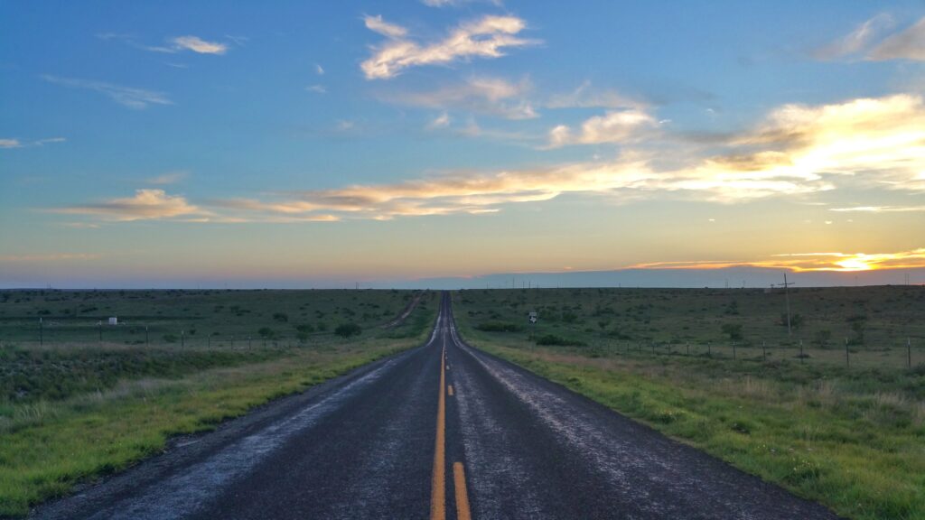 Long road through green field at twilight with dramatic clouds soft sunlight peaceful landscape Wallpaper