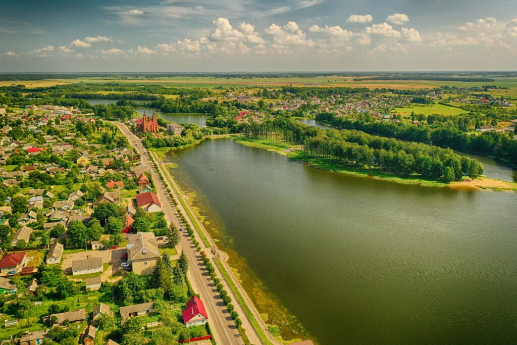 Aerial view of peaceful village by winding river with lush greenery and bright cloudy sky wallpaper