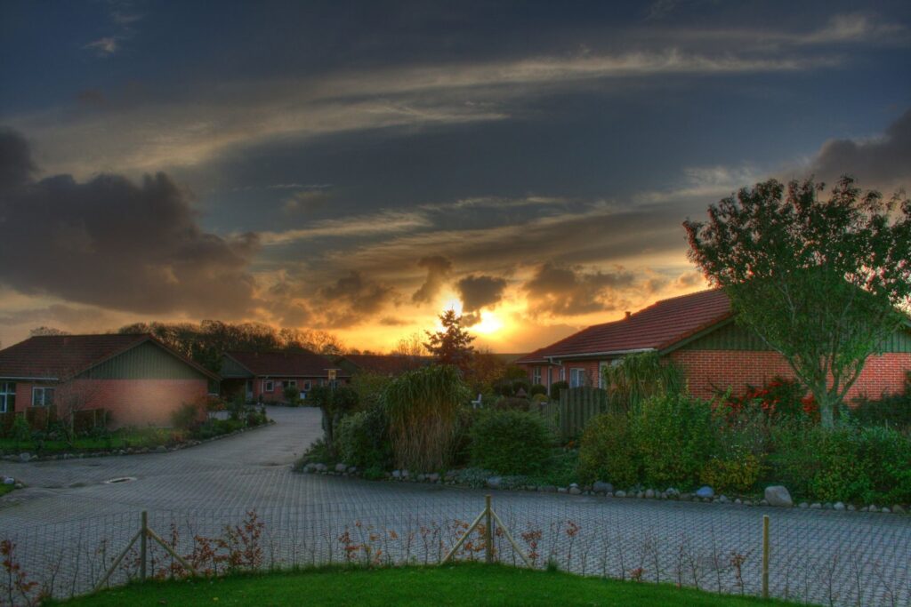 Sunset village scene with red roofs cobblestone road and warm light through dramatic clouds Wallpaper