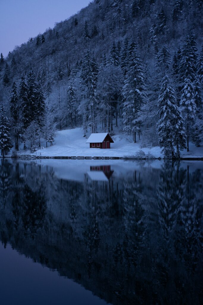 Winter landscape with red cabin snow-covered trees lake reflection peaceful nature wallpaper