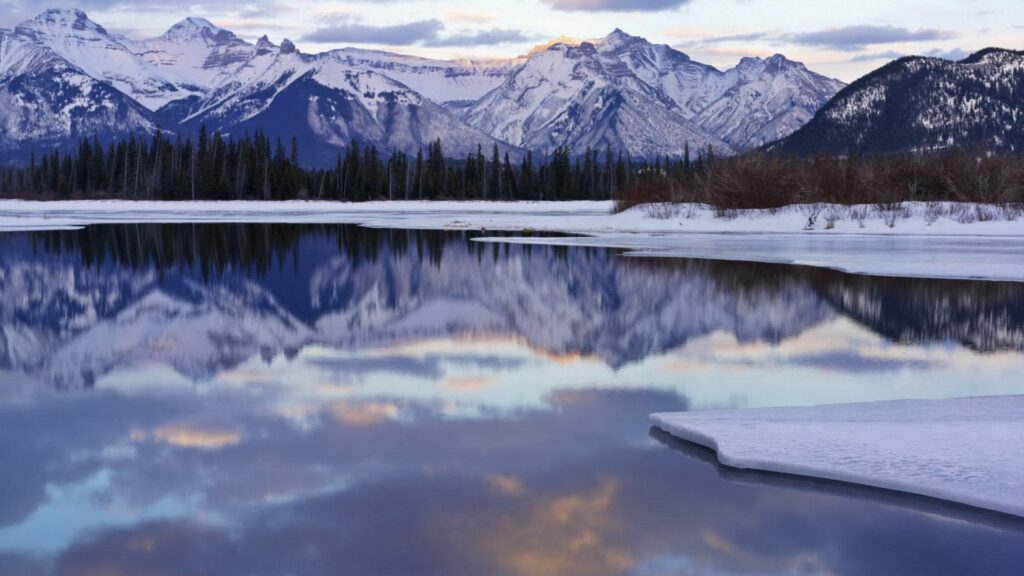 Winter landscape wallpaper icy water reflecting snow mountains pastel sky serene wilderness