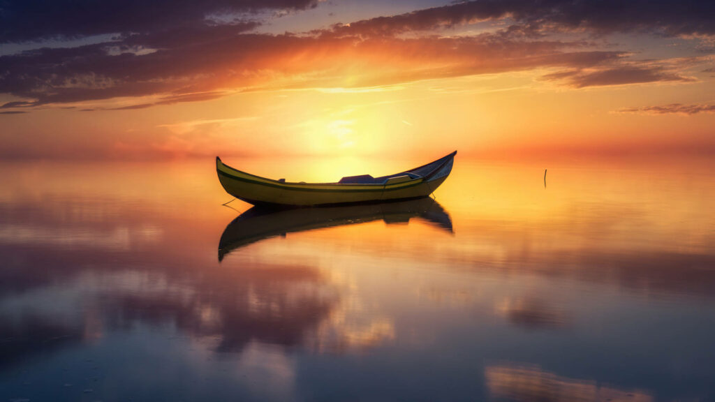 Yellow boat peacefully floating on calm water reflecting vibrant sunset sky wallpaper background