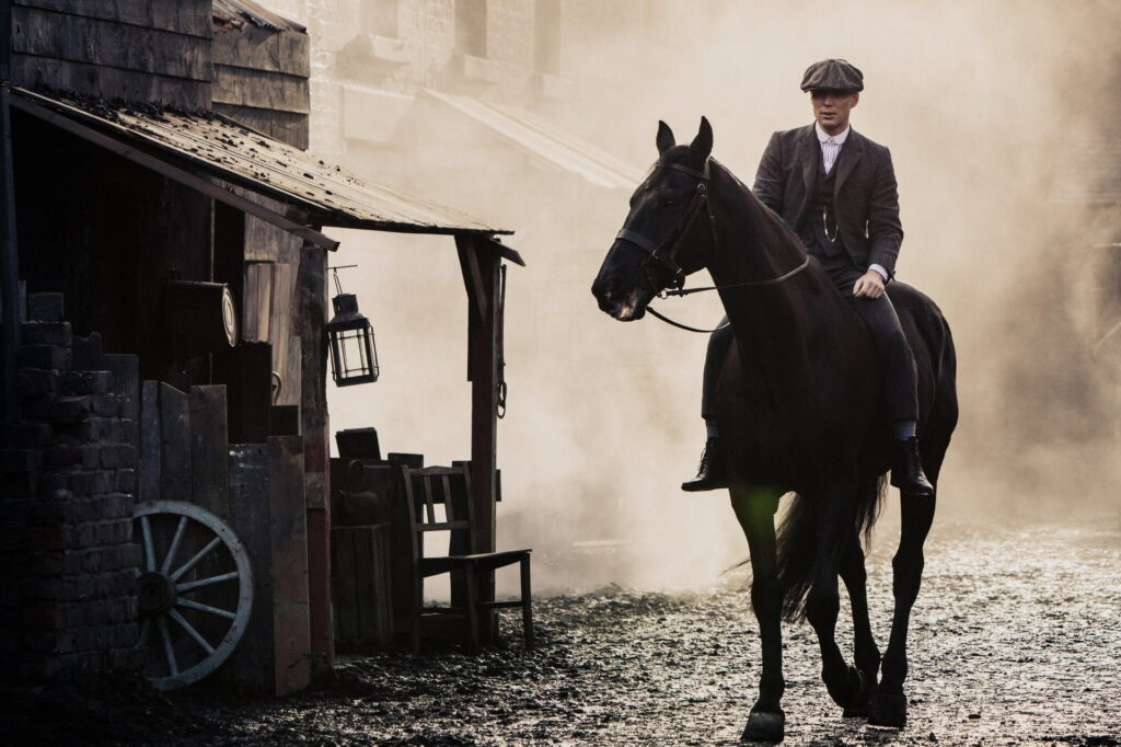 Riding Through History: Thomas Shelby, the Iconic Gangster of Peaky Blinders, on Horseback in Gritty Atmosphere Wallpaper