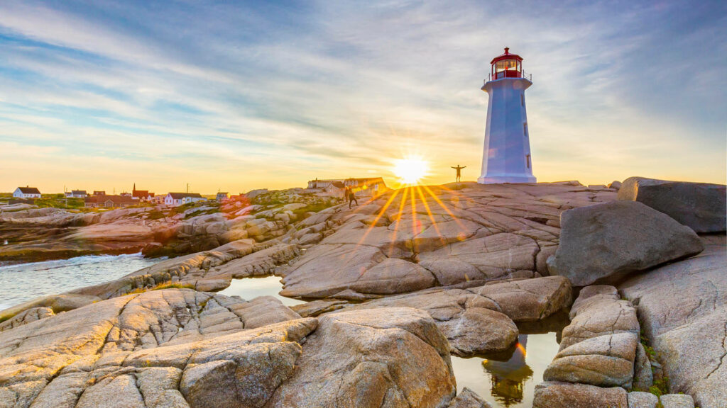 Peggys Cove lighthouse in golden sunlight over granite rocks with clear sky coastal wallpaper background