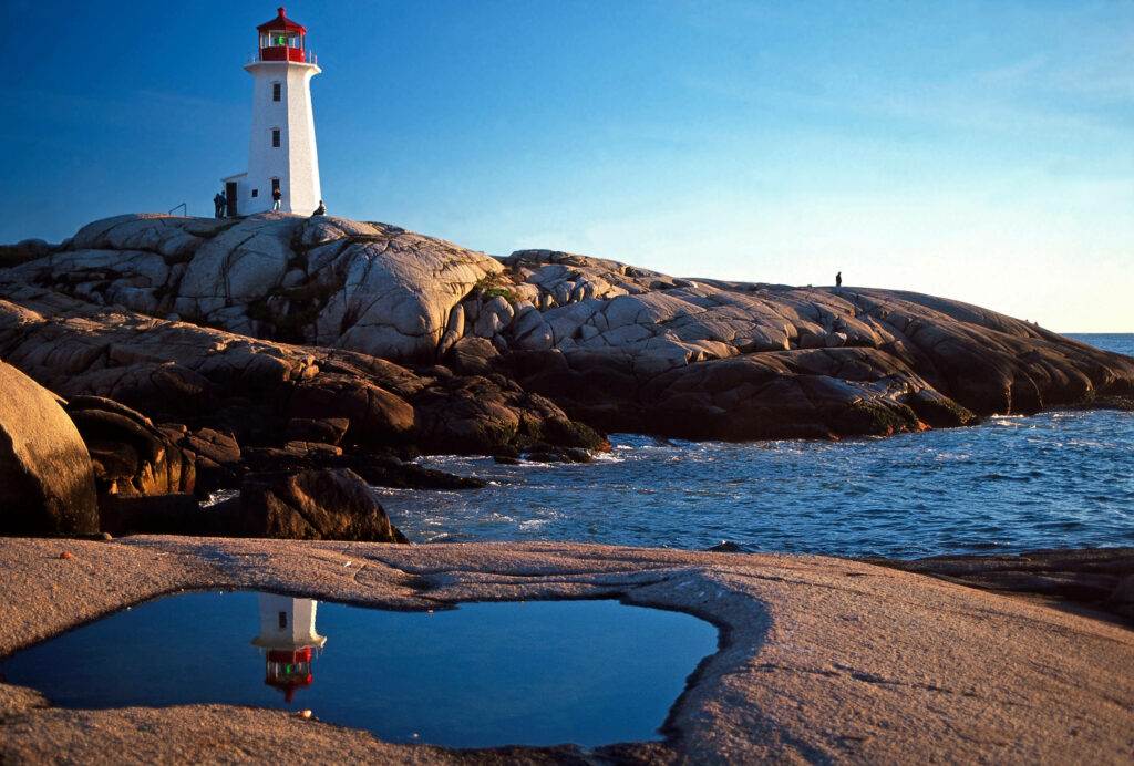 Peggys Point Lighthouse on granite rocks under blue sky with sunlight reflecting on tidal pool Wallpaper