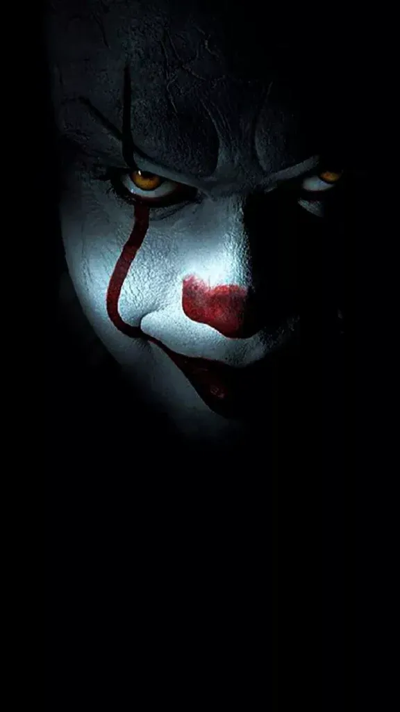 Close-up of Pennywise clown with cracked skin amber eyes and red makeup Stephen King It wallpaper