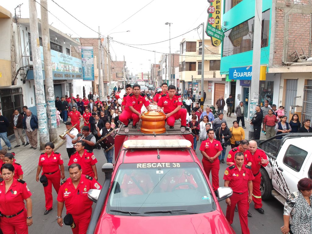 Peruvian volunteer firefighters in red uniforms escort coffin on Rescate 38 vehicle in funeral procession Wallpaper