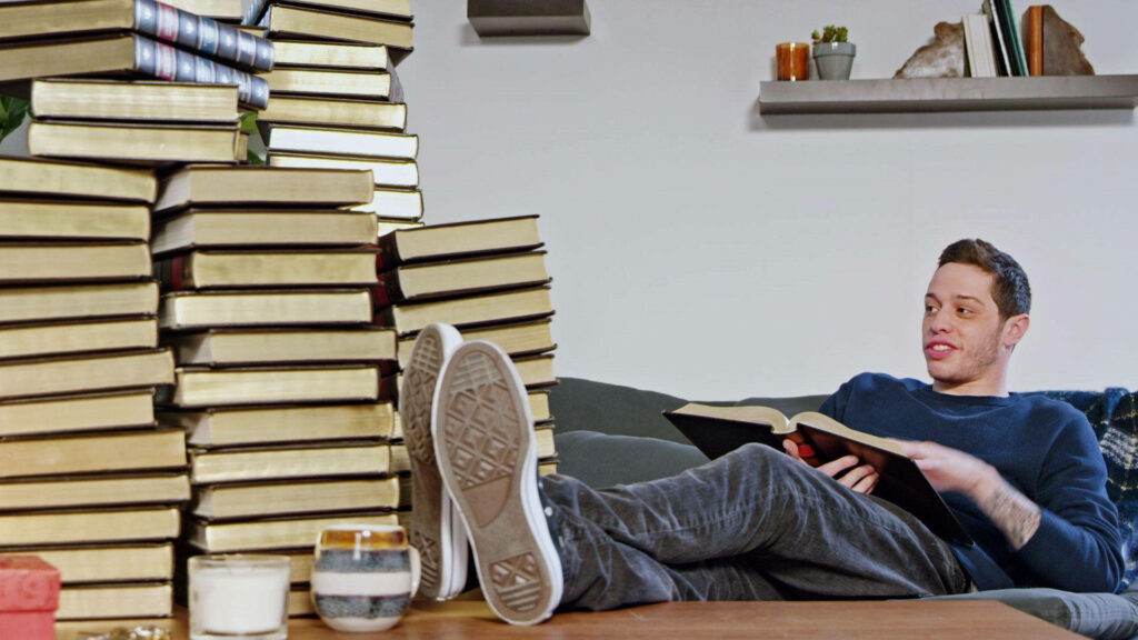 Pete Davidson Relaxing on Couch with Books – Stylish Wallpaper
