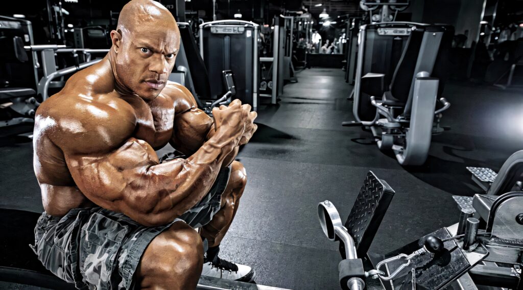 Bodybuilder Phil Heath flexes muscular physique with determined expression in gym with equipment Wallpaper