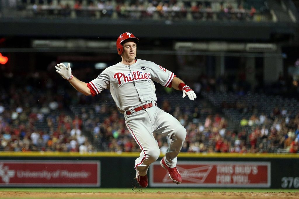 Philadelphia Phillies player in grey uniform jumping mid-air during intense base play stadium lights Wallpaper