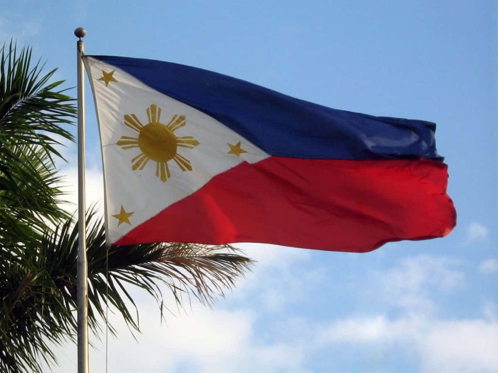 Philippine flag waving against blue sky with tropical palm tree scenic patriotic wallpaper background