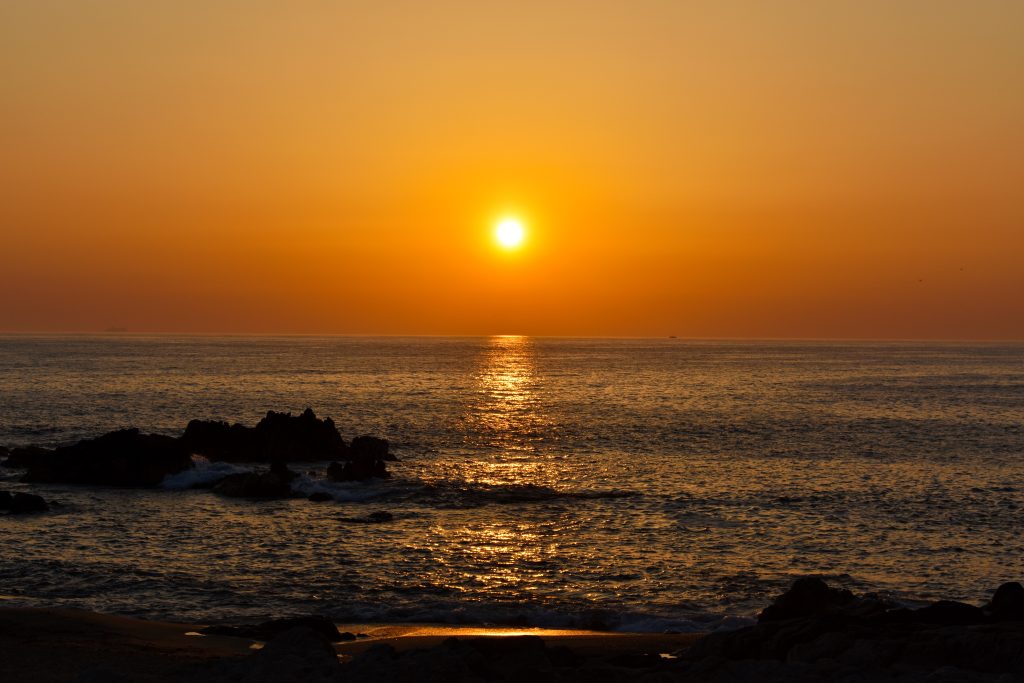 Golden sunset seascape wallpaper over calm ocean horizon with lens flare shimmering reflection rocks