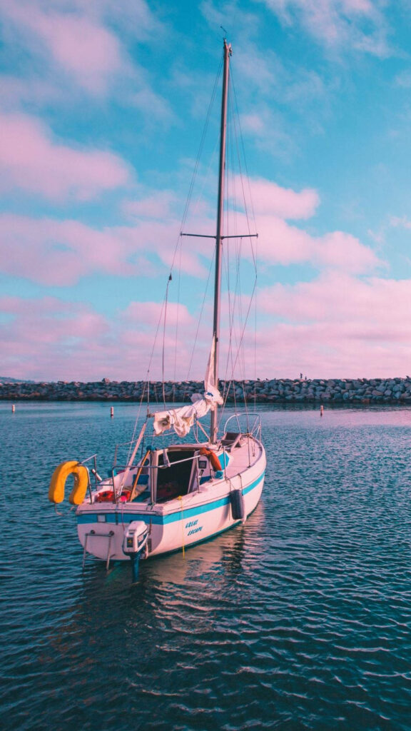Pink Dream: Serene Boat on a Stone Wall Surrounded by Cotton Candy Clouds Wallpaper