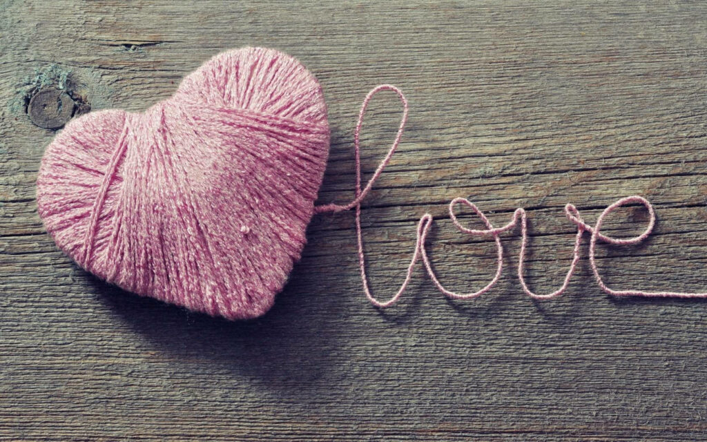 Love Woven with Pink Yarn on a Rustic Wooden Surface Wallpaper