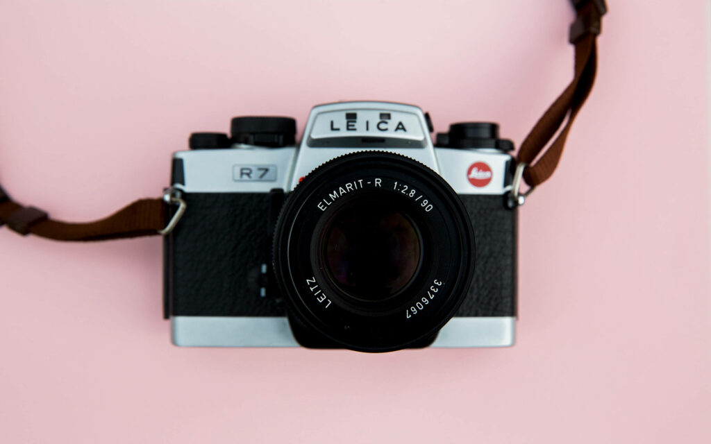 Capturing Creativity: A Stylish DSLR Camera on a Pastel Pink Canvas Wallpaper