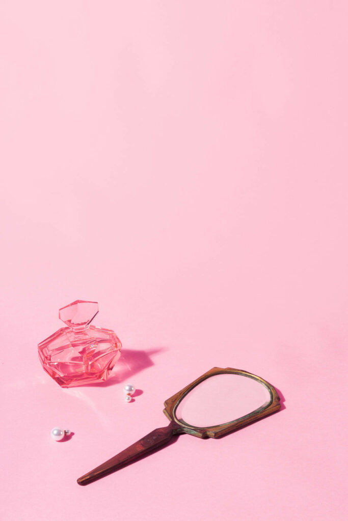 Pastel Elegance: A Whimsical Display of Pink Perfume and Mirror Bliss Wallpaper