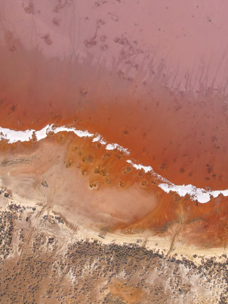 Aerial view of pink sea and sandy shore with white waves creating a pastel coastal scene wallpaper