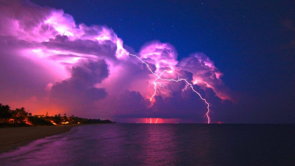 Pink lightning bolt strikes magenta storm clouds over dark ocean nighttime coastal storm wallpaper