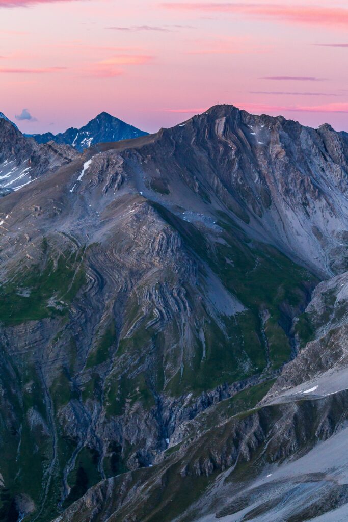 Dramatic mountain peaks at pink twilight with rugged rock textures and green earthy slopes wallpaper