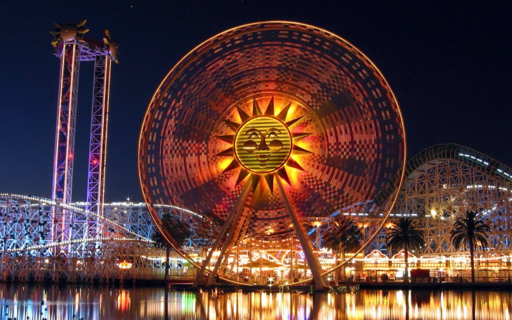 Night view of Pixar Pal-A-Round with glowing sun face and vibrant light trails at Pixar Pier Wallpaper