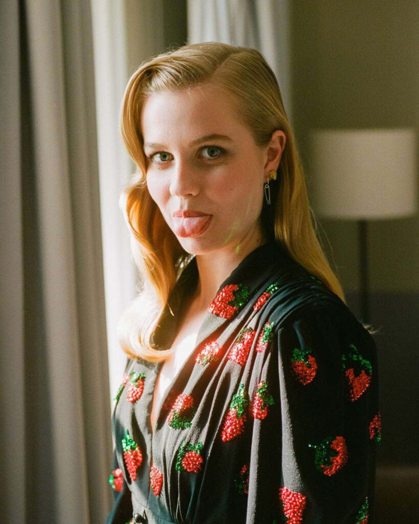 Playful portrait of Angourie Rice posing with tongue out in black outfit with red and green patterns Wallpaper