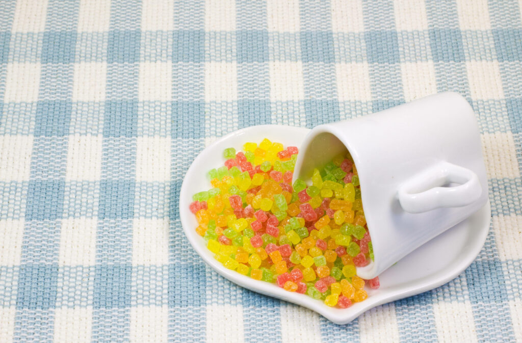 Colorful popping candy spilling from white cup onto heart dish on blue checkered wallpaper background