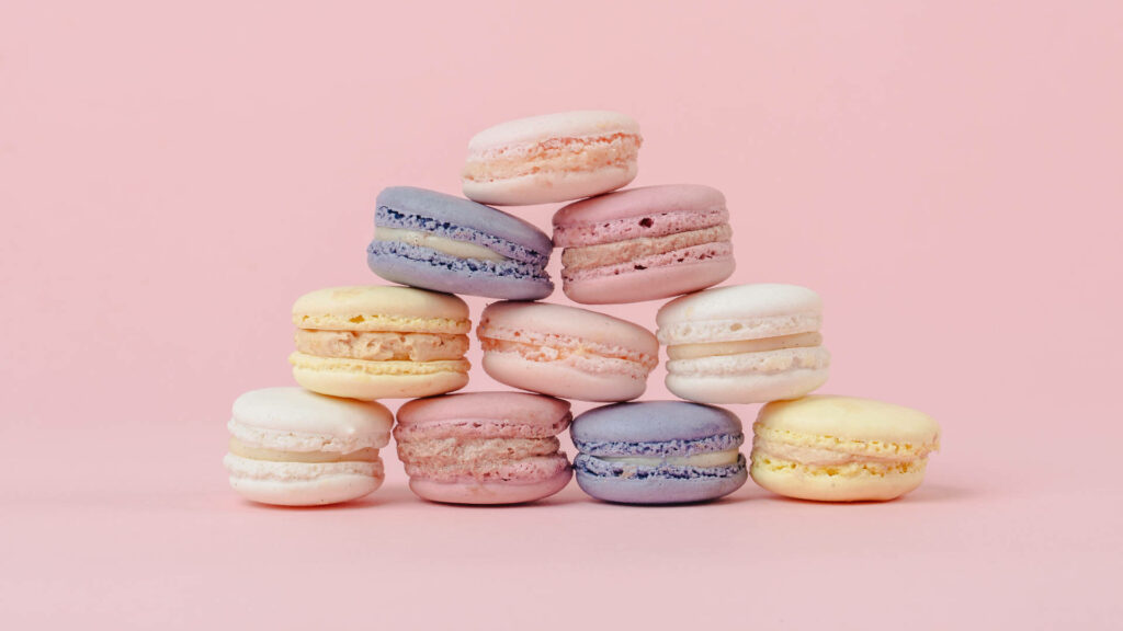 Pastel macarons pyramid in pink lavender yellow on solid pink background wallpaper
