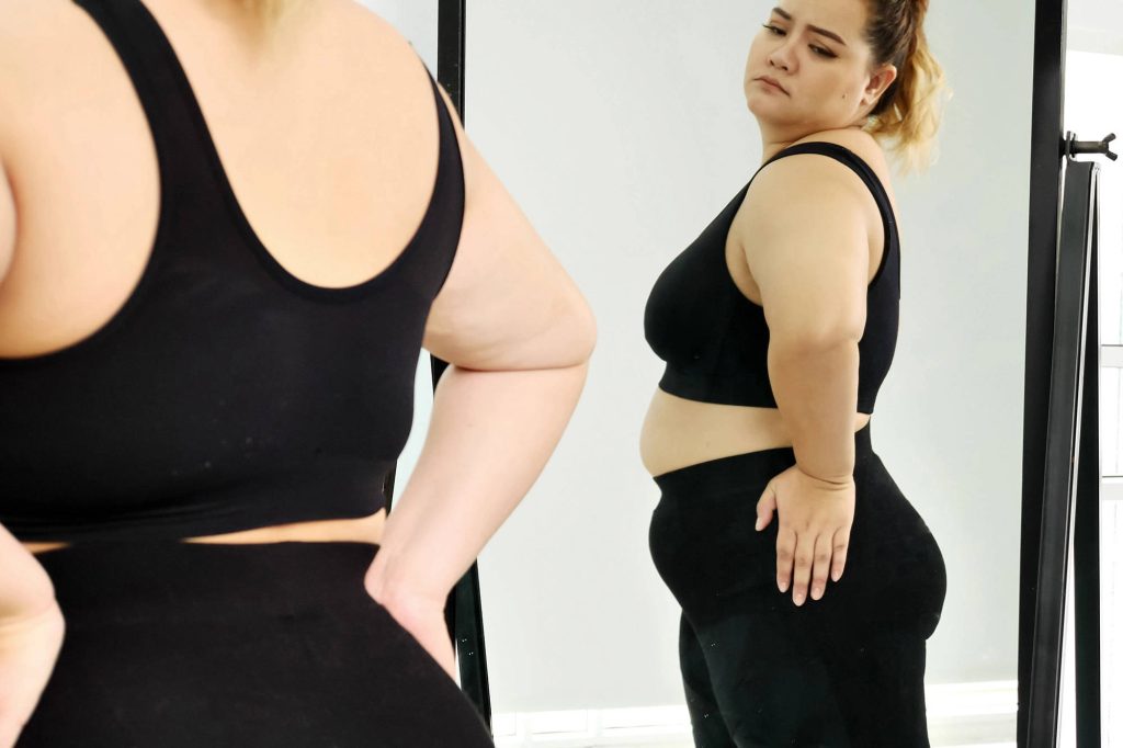 Plus-size woman in black activewear examining reflection in large mirror bright background Wallpaper