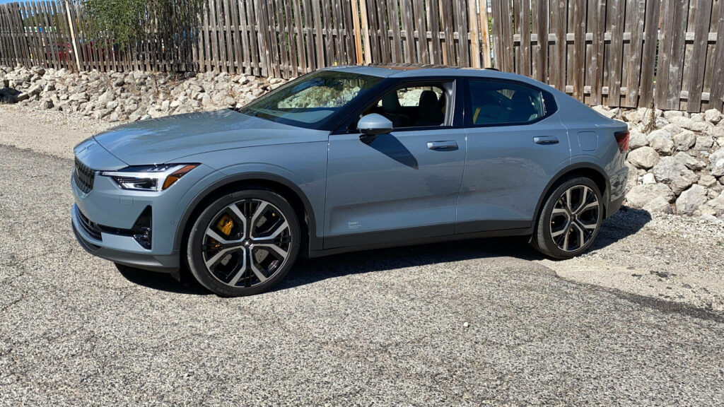 Polestar 2 parked in bright sun with sleek silver body rustic fence and rocky landscape background Wallpaper
