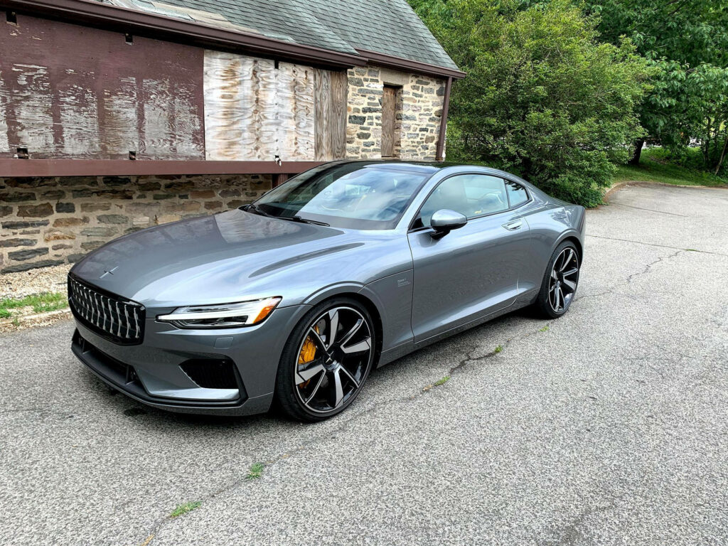 Polestar electric car parked by rustic stone building with lush greenery and cloudy sky background Wallpaper
