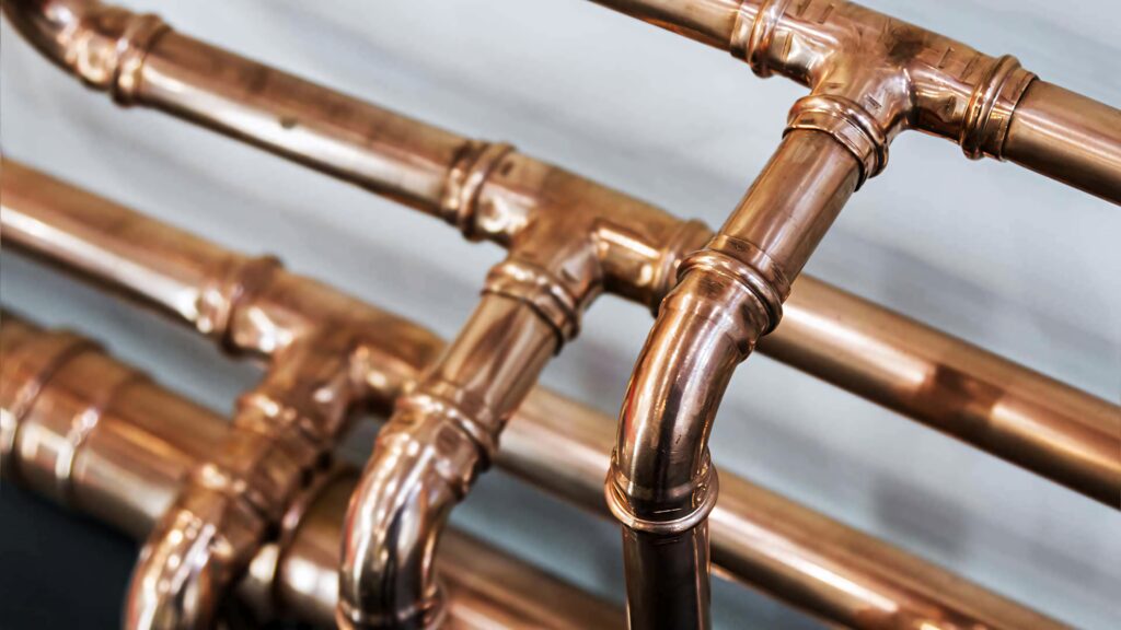 Close-up of polished copper pipes with detailed bends and joints on blurred industrial background Wallpaper