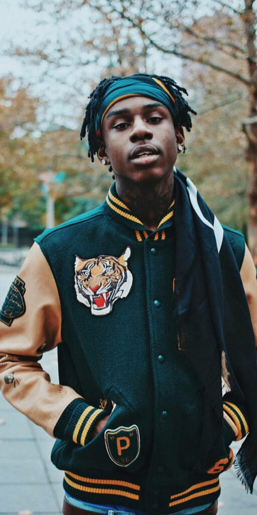 Portrait of rapper Polo G in green varsity jacket with tiger patch and headband outdoors Wallpaper