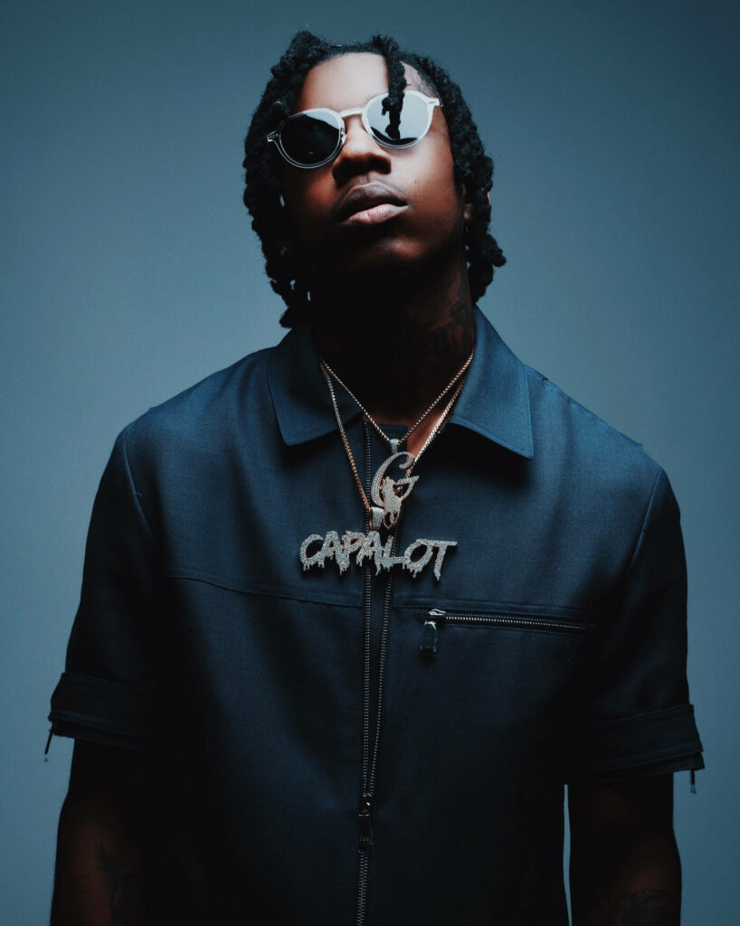 Moody portrait of rapper Polo G in sunglasses with CAPALOT diamond chain blue studio lighting wallpaper