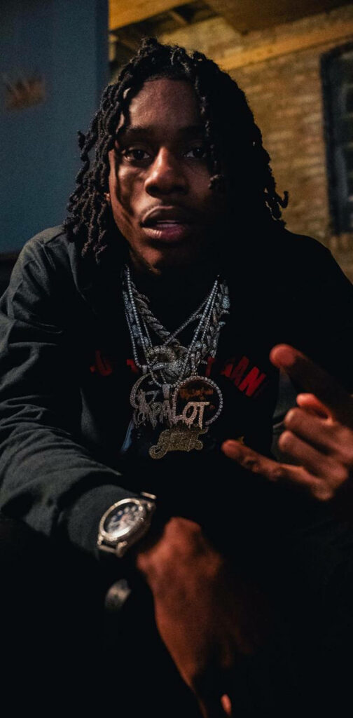 Moody portrait of rapper Polo G with dreadlocks and diamond chains on dark industrial background Wallpaper