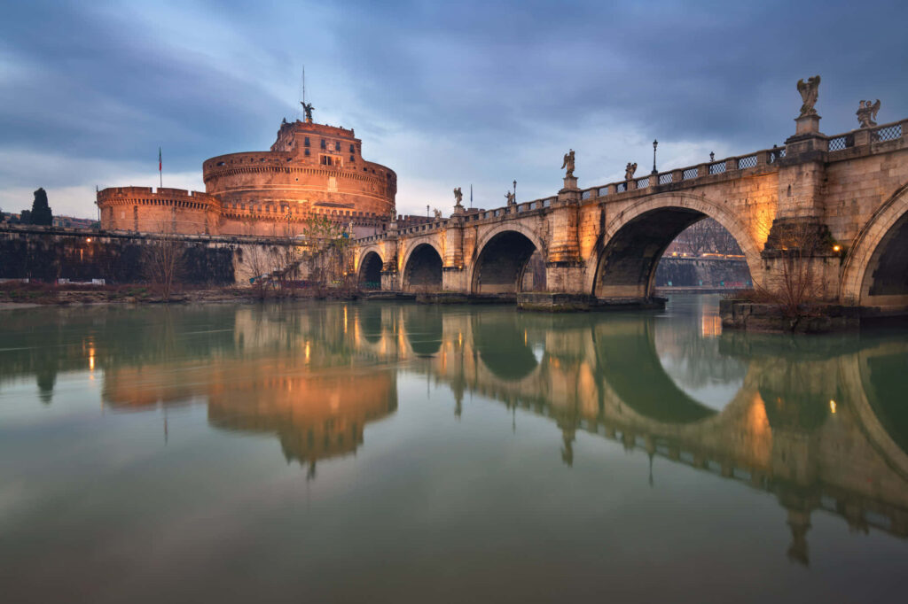 Ponte Sant Angelo and Castel Sant Angelo in Rome at dusk with golden lights reflecting on Tiber River Wallpaper